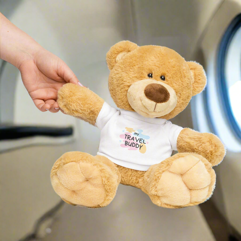 Teddy bear wearing a 'My Travel Buddy' shirt with a hand holding its paw on a white background