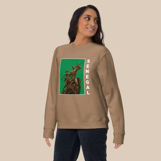 Model wearing a tan crewneck sweatshirt with an African Renaissance Monument graphic on green and white vertical Senegal lettering.
