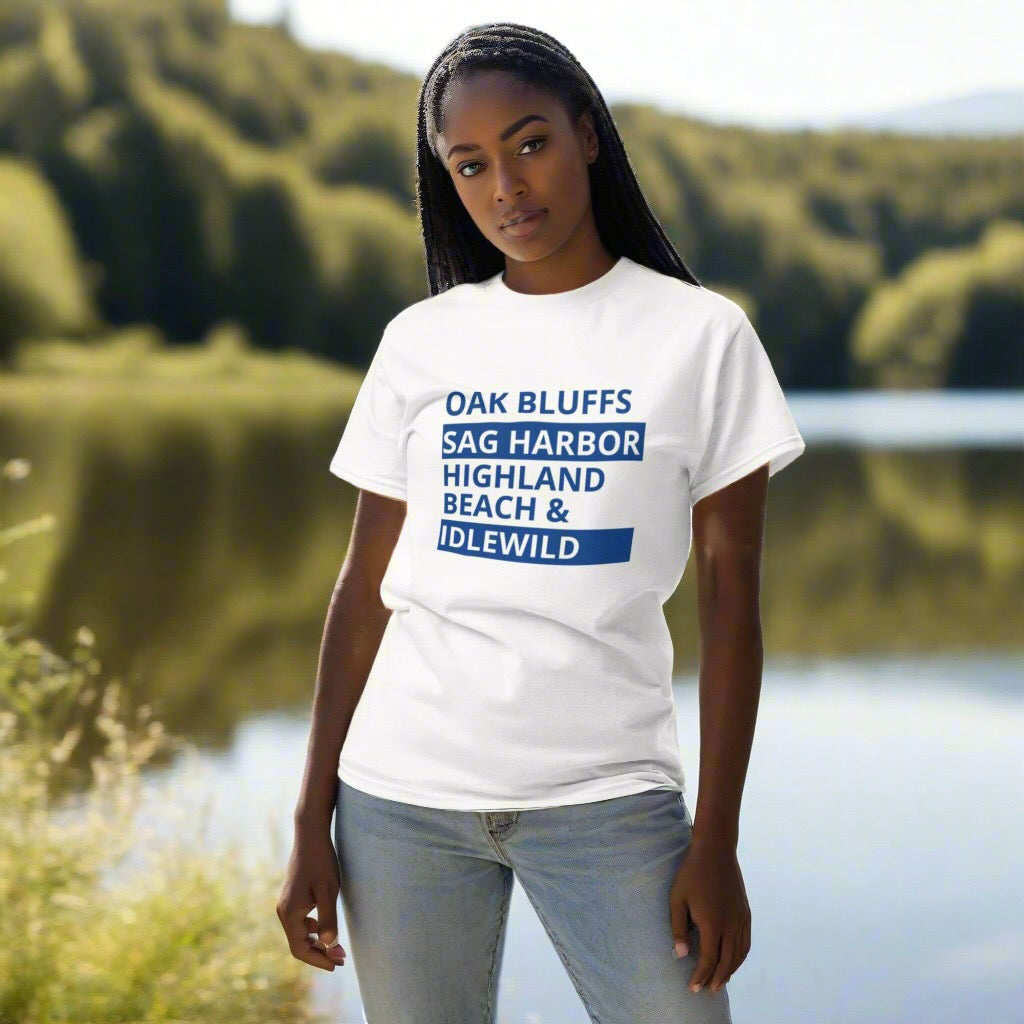 Person wearing a white t-shirt with text standing by a lake with greenery.